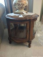 Full view of round wooden display side table with glass door and carved details