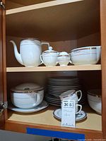 cabinet view showing teapot, sugar bowl, creamer, covered tureen, stacked plates, cup
