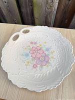 Top view of round white porcelain platter with pastel floral centre and leaf-embossed rim