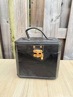 Front view of closed black faux leather jewelry case showing gold-tone latch and handle