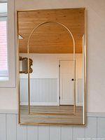 Full view of gold framed rectangular mirror with arched inner frame hung on wall