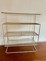 Front view of gold metal shelf showing three mesh tiers and frame