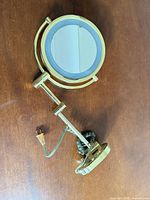 Front view of gold/brass lighted vanity mirror showing mirror face and swivel arm
