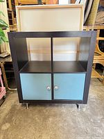 Front view showing four cubbies, two blue doors, silver knobs, silver legs