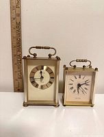 Front view of both brass and glass carriage clocks beside ruler