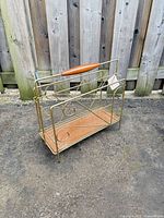 Overall view of brass-tone magazine rack showing metal frame, teak handle, teak base