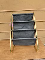 Front view of brass frame magazine rack with four black fabric pockets