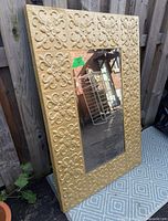 Full view of ornate gold framed mirror leaning against fence