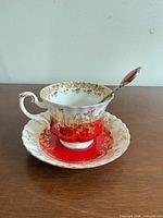 Teacup on saucer with spoon resting inside, showing red and gold gilt pattern