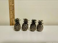 Front view of four silver-plated pineapple card holders with ruler for scale