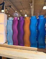 Six frosted glass wavy vases in assorted colours lined on a wooden shelf