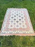 Full view of ivory, blush and gray flatweave rug on grass
