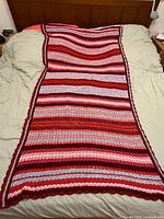 Full length view of crocheted afghan laid on bed showing stripe pattern and scalloped border