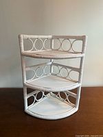 Front view of white rattan three-tier corner shelf