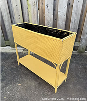 front angled view showing yellow wicker planter box, black interior, lower shelf