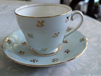 Teacup on saucer showing exterior color, gilt leaves and gold trim