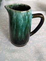 Side view of Blue Mountain Pottery creamer pitcher showing green and black drip glaze, handle and spout