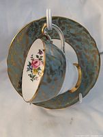 Teacup hanging on saucer showing exterior sage green with gold scroll and interior floral bouquet