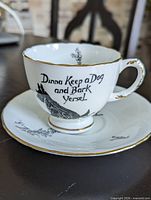 Teacup on saucer showing graphic, text and gold trim detail