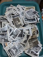 Bin filled with hundreds of small black-and-white photographs, stacked loosely