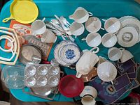 Top view of entire assortment showing tea set pieces, utensils, bakeware, plates, pamphlets, and fabric