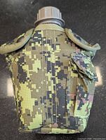 Front view of camo-covered army canteen showing cap, snap closures, side pouch