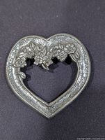 Front view of heart-shaped pewter brooch showing floral motif and open centre