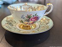 side view of teacup on saucer showing mint-green ground, fruit and floral centre and gold filigree