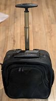 Front view showing entire black rolling carry-on with extended T-handle, wheels and exterior pockets visible