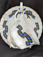 Teacup hanging in front of saucer showing tartan pattern and crest