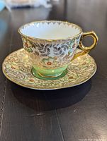 Teacup on saucer showing pattern, green footing, gold gilding