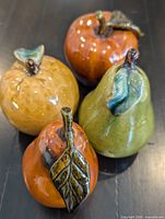 Group shot of four ceramic fruit figurines—three apples and one green pear—on table