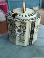 Front/side view of hexagonal Noritake porcelain jar with lid showing floral and geometric decoration and gold finial