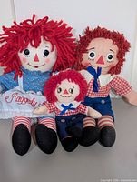 Three cloth Raggedy plush dolls seated together showing size and outfits