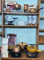 Overview of shelving with multiple fondue pots, stands, plates and boxed accessories