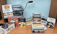 Group shot of both pasta machines, cutter attachments, herb grinder, boxes and manuals