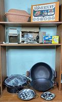 Full lot on shelving: clay baker, box, electric grinder, meat grinder, woks, egg poacher pan