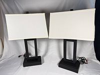 Front view of both black metal table lamps with white rectangular shades, cords visible