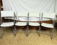Front view of all four white metal folding chairs lined up