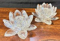 Two clear crystal lotus candlestick holders on wood surface