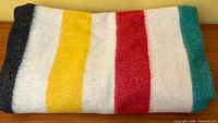 Folded blanket showing stripe pattern black, yellow, white, red, white, teal