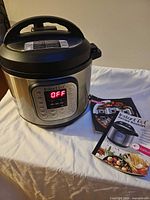 Instant Pot cooker with lid, manuals beside it