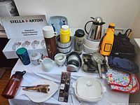 Group shot showing majority of items including Stella Artois glasses, multiple thermoses, utensils, textiles, trays and boxed items