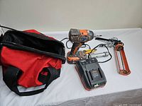All items laid out: impact driver with battery, charger, caulking gun, utility knife, tool bag