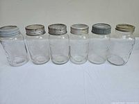 Six clear glass mason jars with metal lids lined up