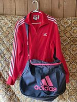 Red Adidas track jacket and black duffel bag together