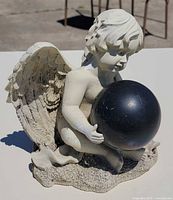 Front left view of seated cherub holding black orb
