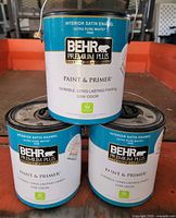 Three sealed Behr Premium Plus paint cans front labels visible