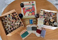 Overview of entire lot on table: two boxes of thread spools, Singer book, yarn cards and notions