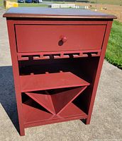 Front view of maroon wooden wine storage cabinet showing drawer, stemware rack slots, shelf, and X bottle rack